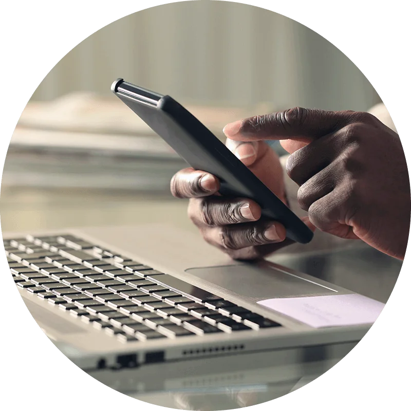 Hand holding a mobile phone in front of a computer.